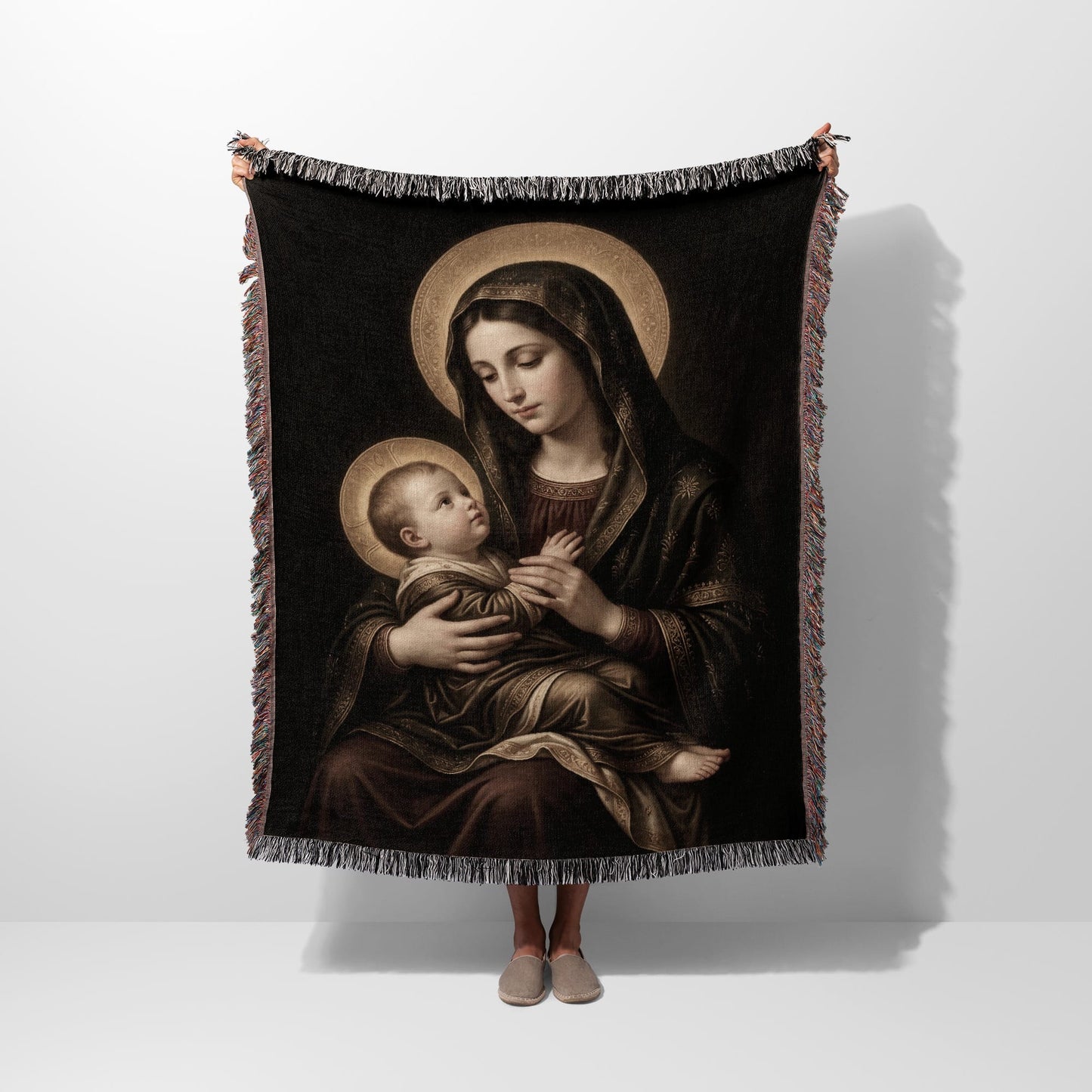 Tapestry depicts Virgin Mary holding baby Jesus, both with halos, against a dark background.