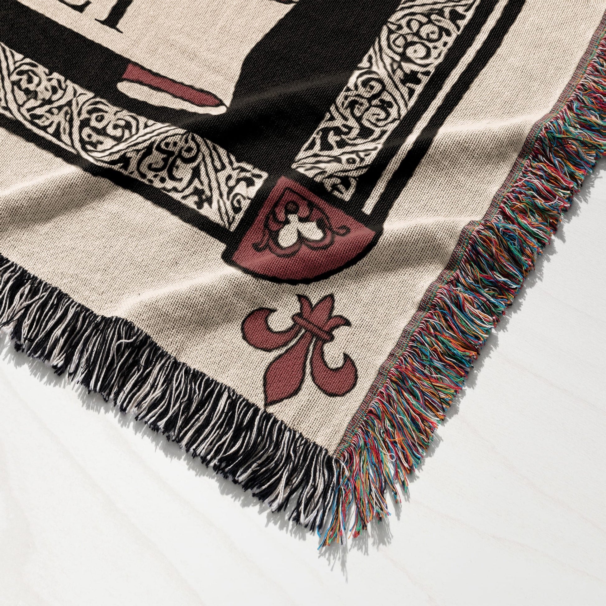 Woven blanket with fleur-de-lis and ornate border design, frayed edges.