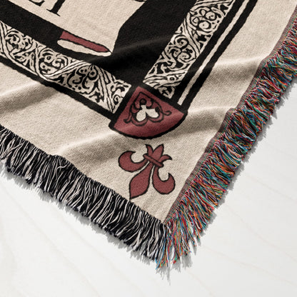 Woven blanket with fleur-de-lis and ornate border design, frayed edges.