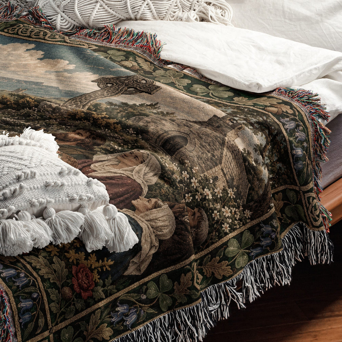 A woven throw blanket with a Renaissance art scene draped over a bed with white pillows.