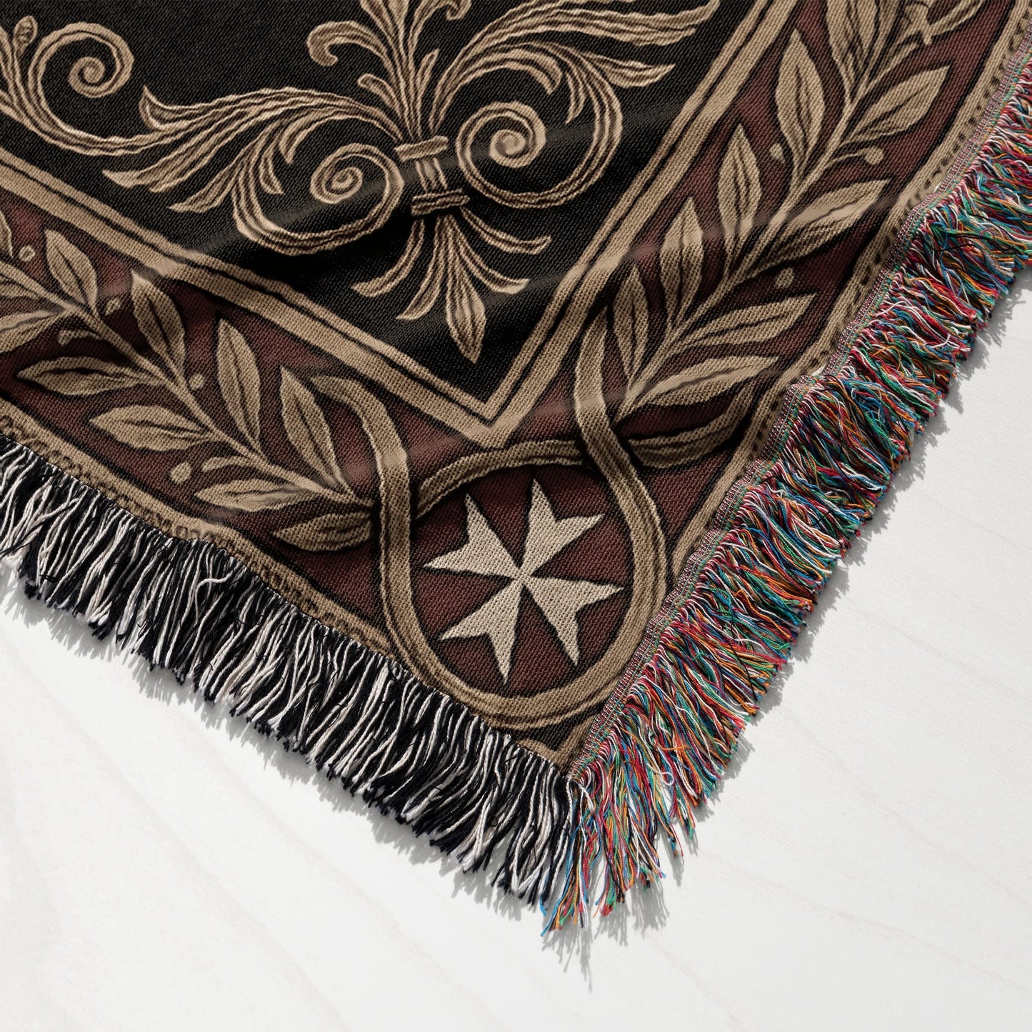 Dark patterned throw blanket with fringe and a central Maltese cross motif.