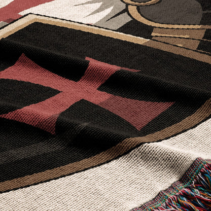 Knitted blanket featuring a black shield with a red cross and decorative fringe.