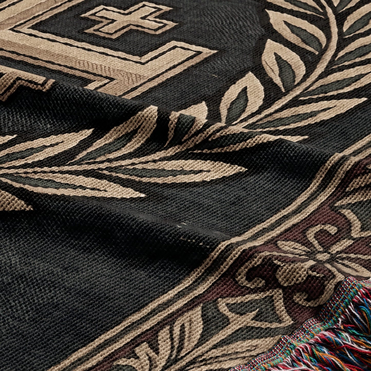 Dark woven blanket with tan geometric and laurel leaf patterns and fringed edge.