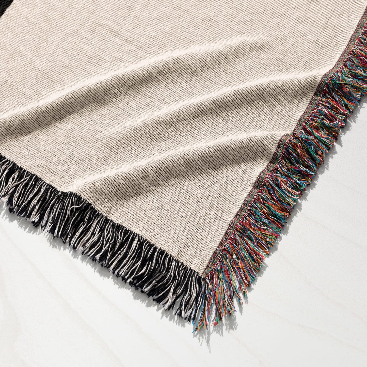 Textured cream woven blanket with colorful fringed edges on white surface.
