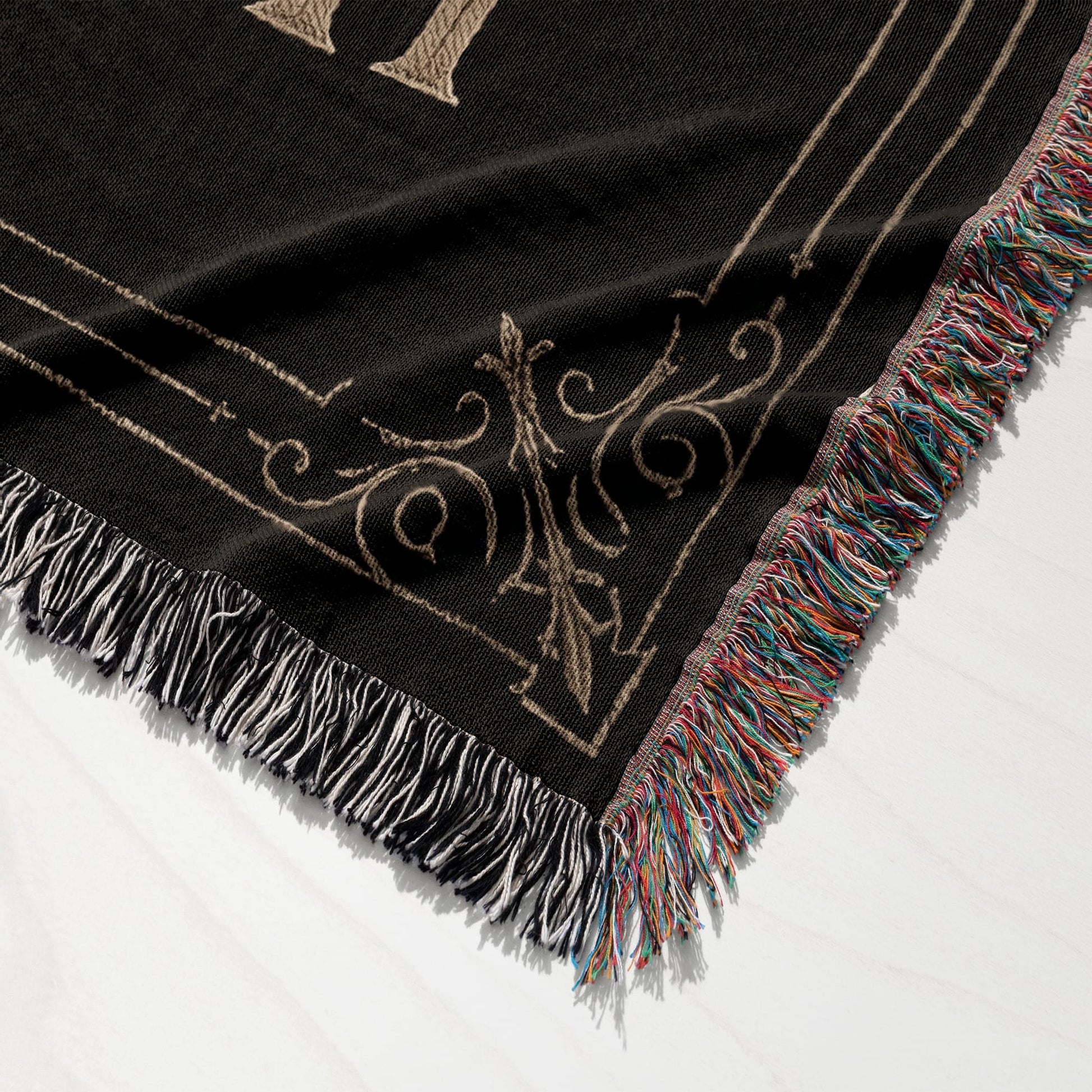 Black woven throw blanket with ornate tan pattern and multicolored fringe.