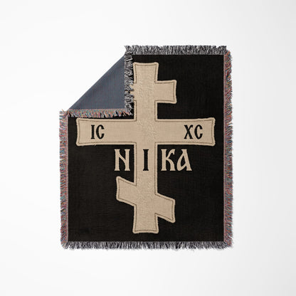 Black woven blanket with a large beige Orthodox cross and Greek text.