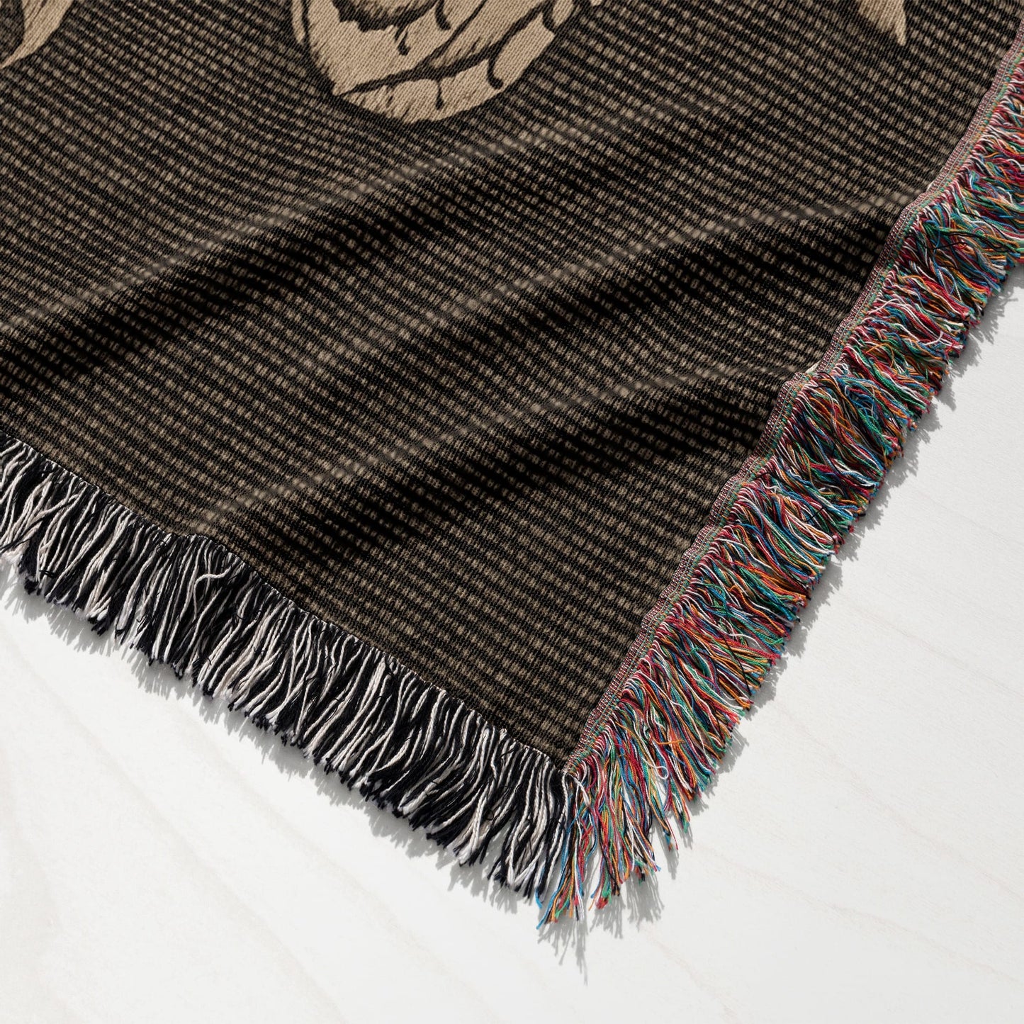 Close-up of woven blanket corner with colorful fringe and floral pattern detail.