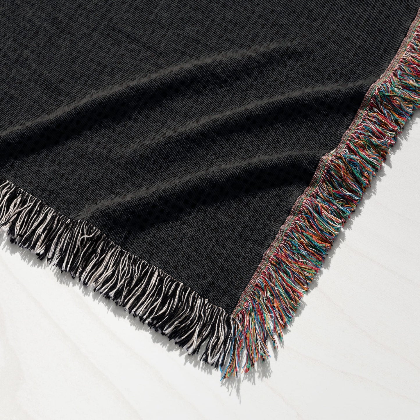 Black woven blanket with fringed edges, showing a detailed texture.