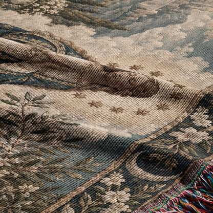 A folded woven blanket featuring a vintage pastoral landscape with foliage and multicolored fringe.