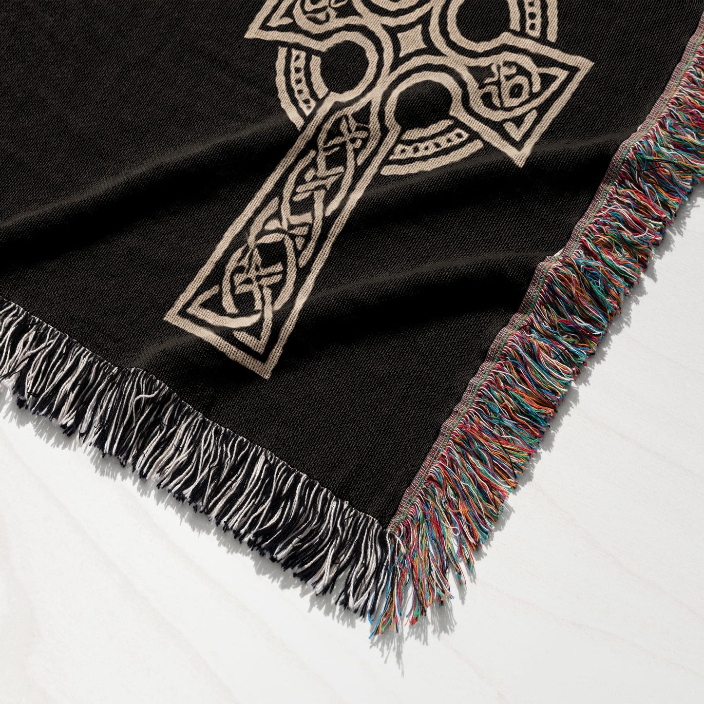 Black woven throw blanket with a beige Celtic knot cross and colorful fringed edges.