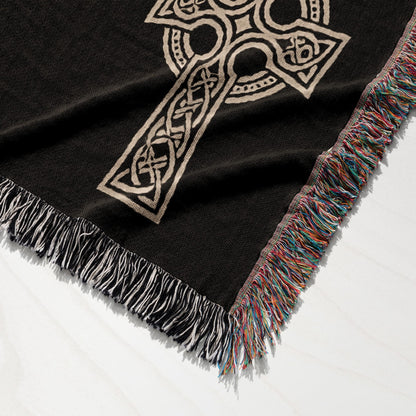 Black woven throw blanket with a beige Celtic knot cross and colorful fringed edges.