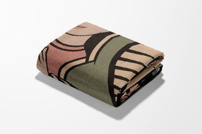 Folded throw blanket with geometric pattern in beige, green, and pink.