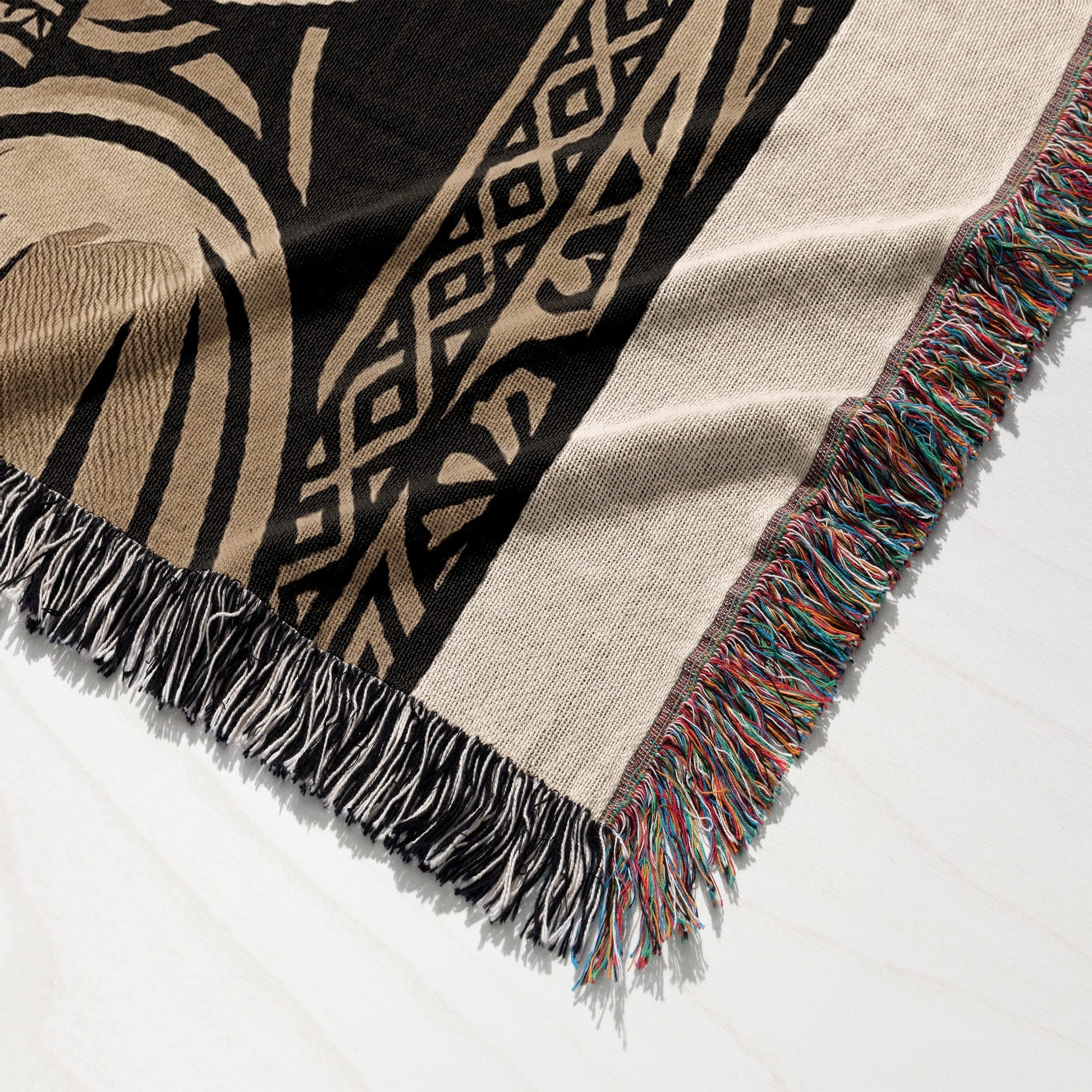 Woven throw blanket with fringe and abstract geometric pattern in tan and black.