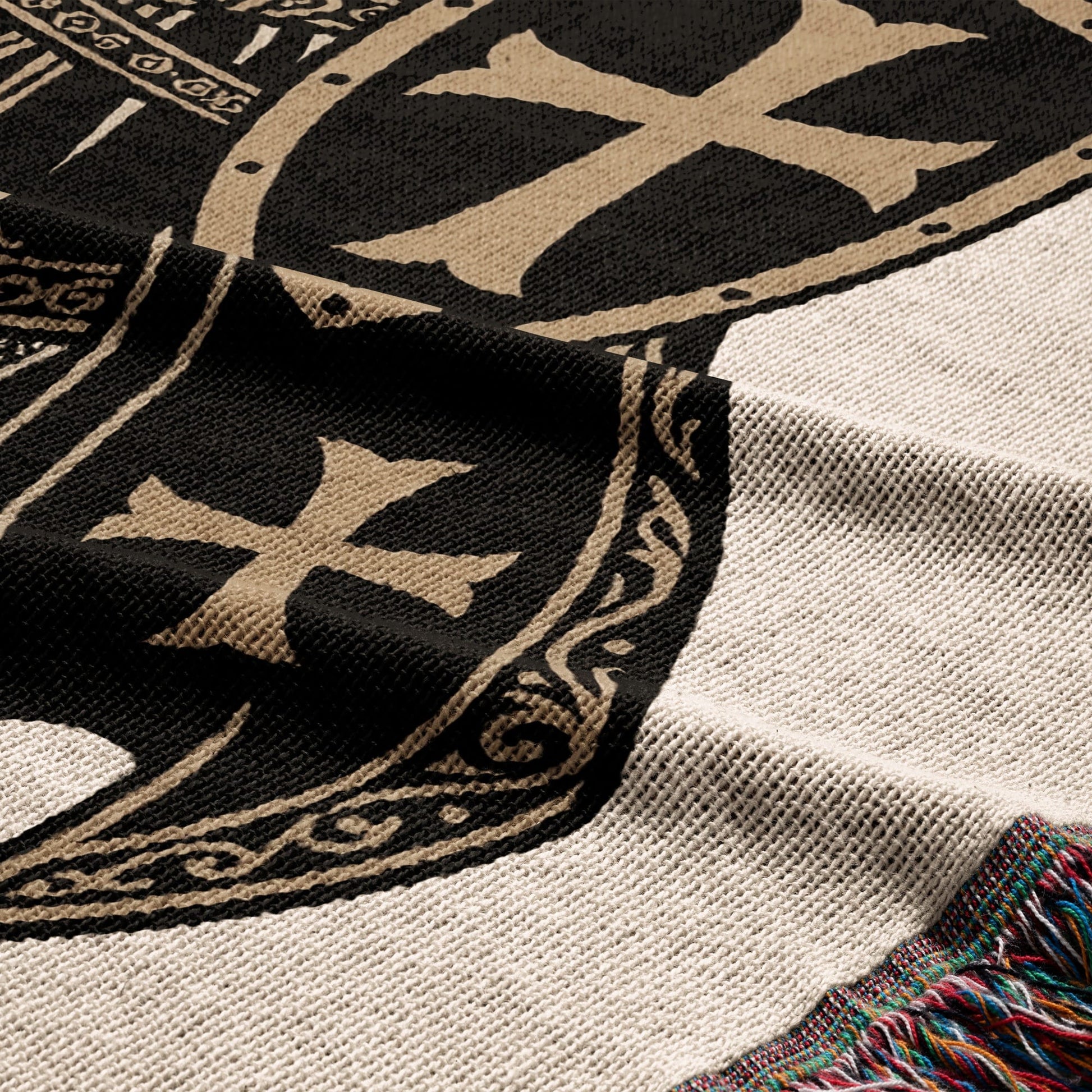 Cream knit blanket with black and gold cross emblem and tasseled edge.