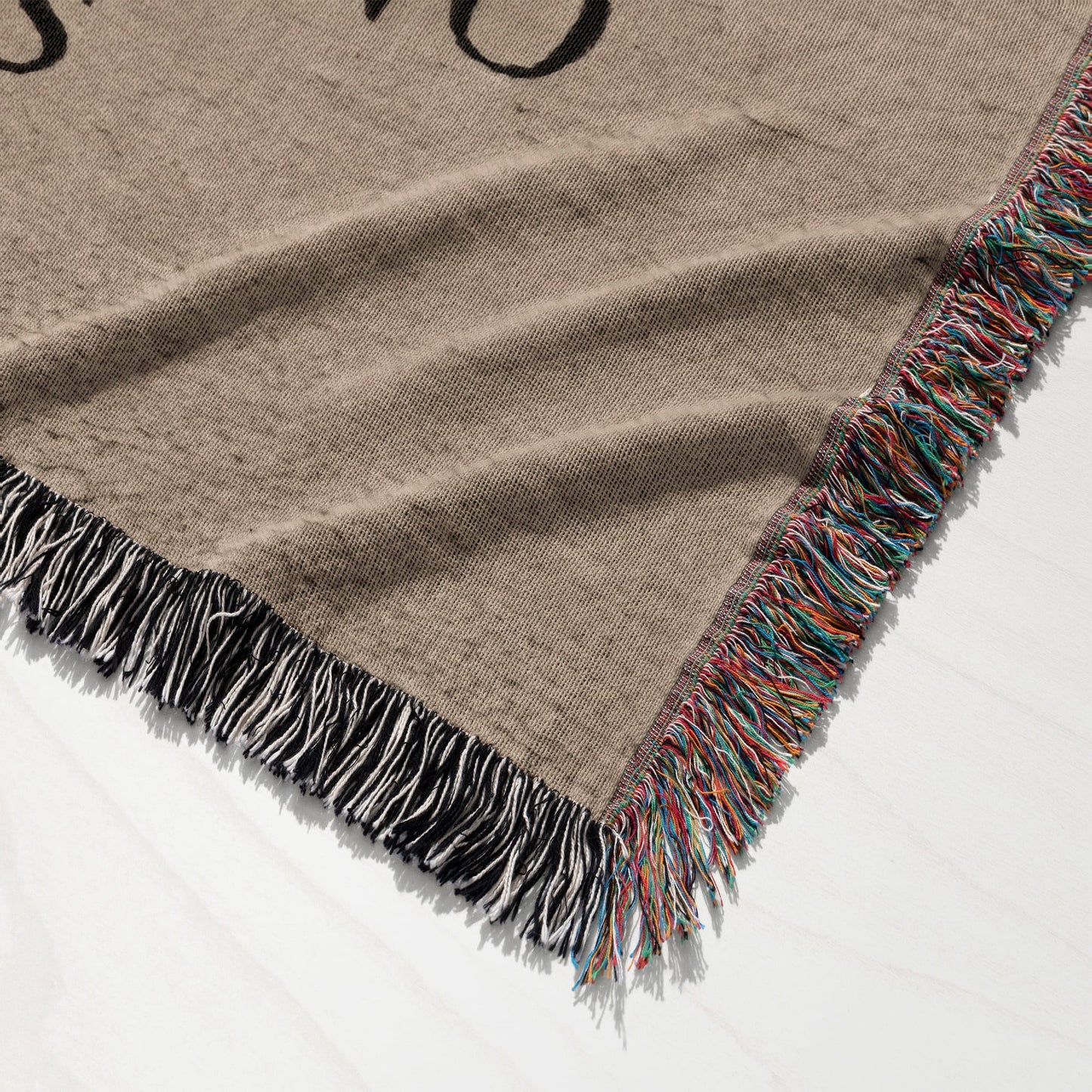 Brown woven blanket with black and white fringe on one side and multicolor fringe on another.