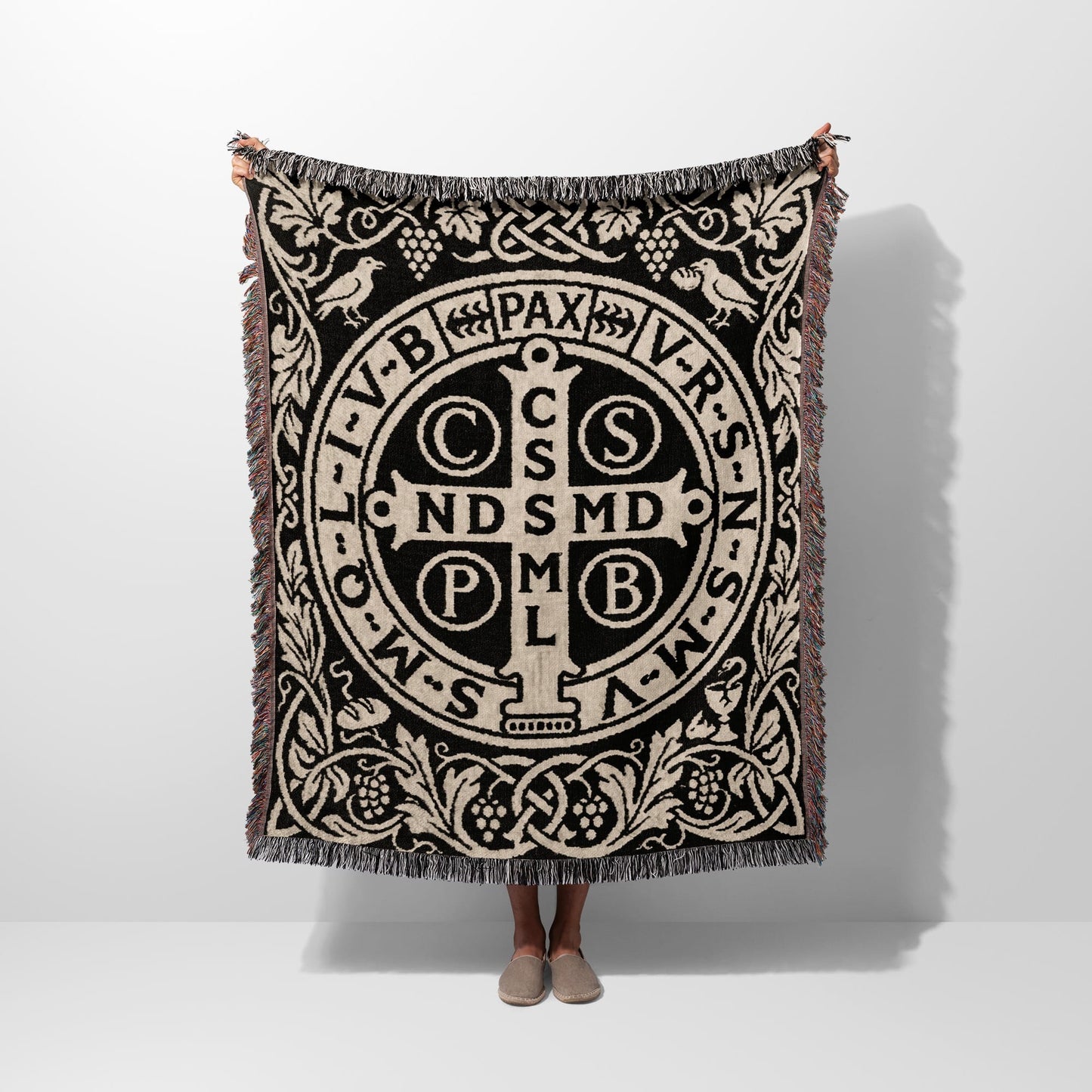 Black and beige woven blanket with Saint Benedict medal design and fringe.