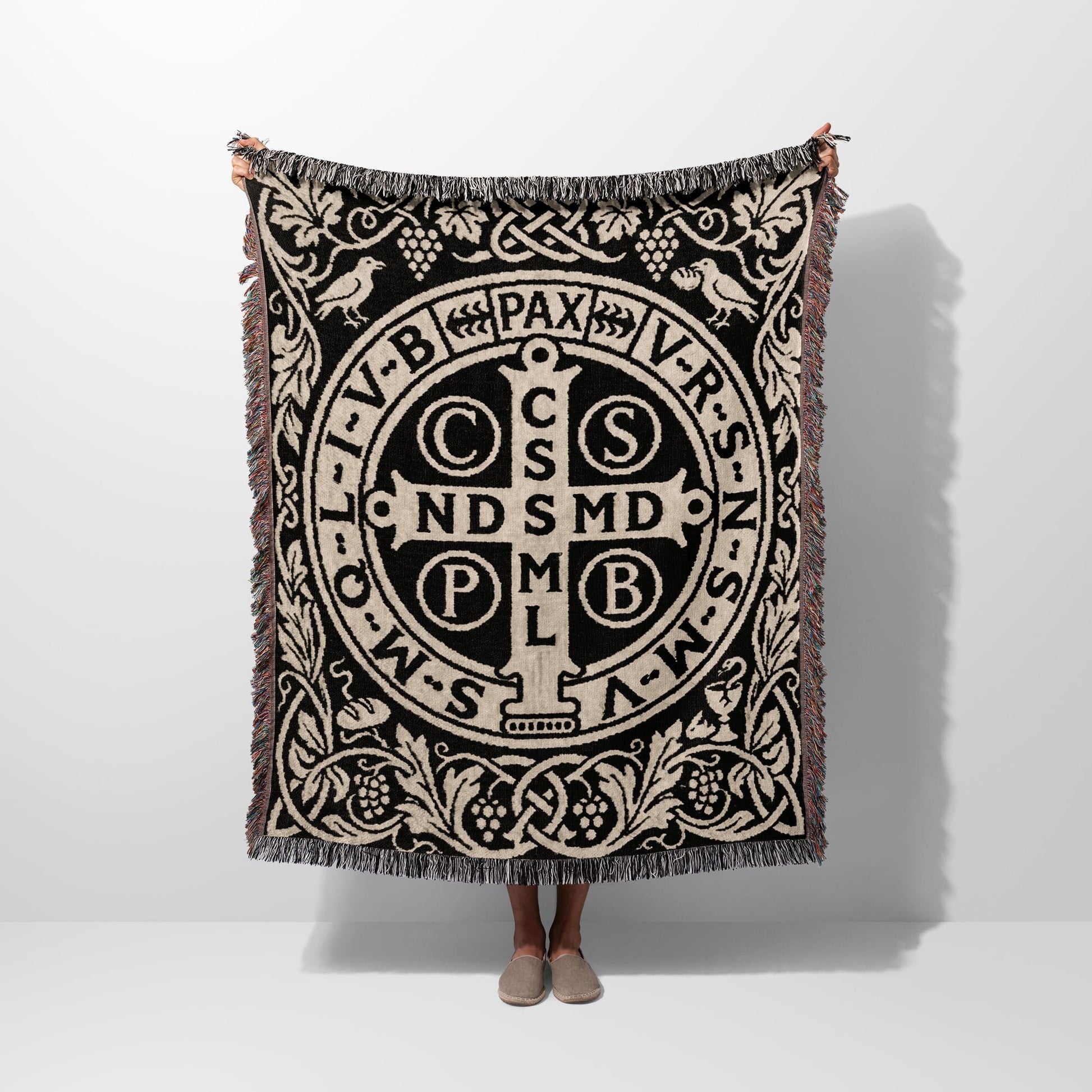 Black and beige woven blanket with Saint Benedict medal design and fringe.