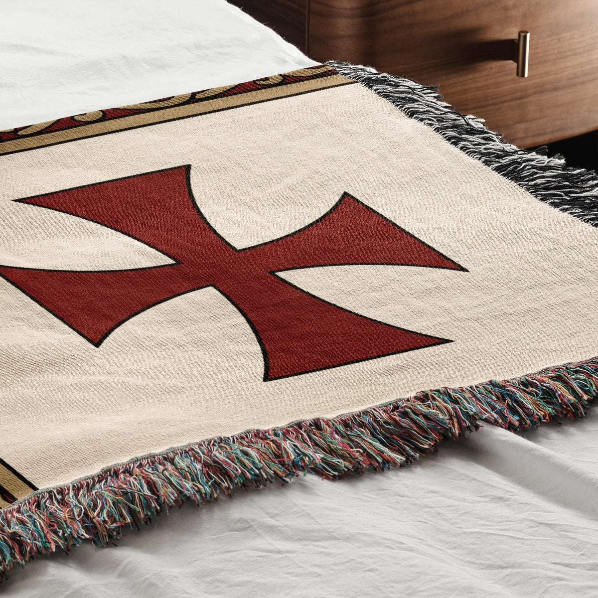 Tapestry with red cross symbol and fringed edges on a bed.