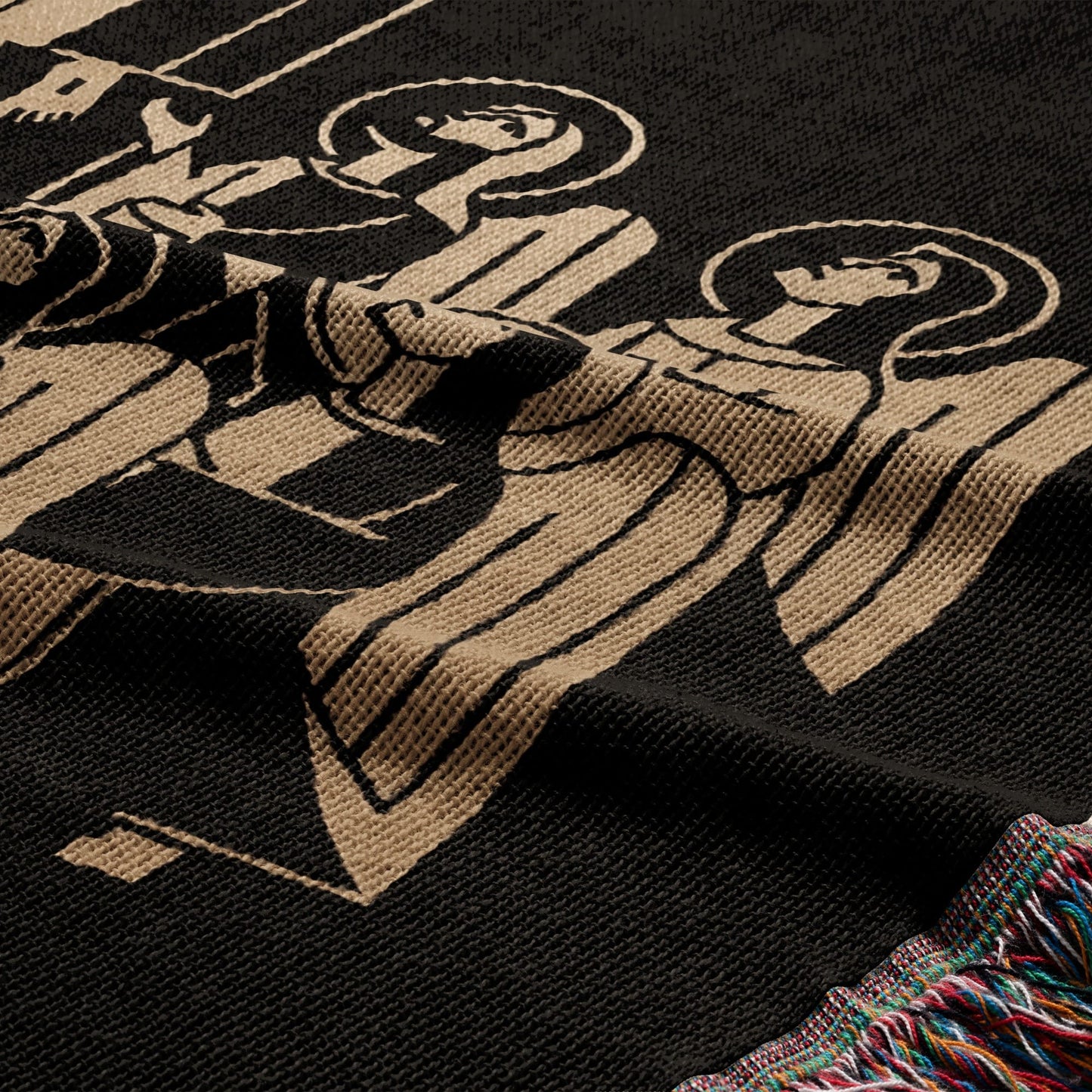 Black woven blanket with tan stylized angelic figures and fringed edge.
