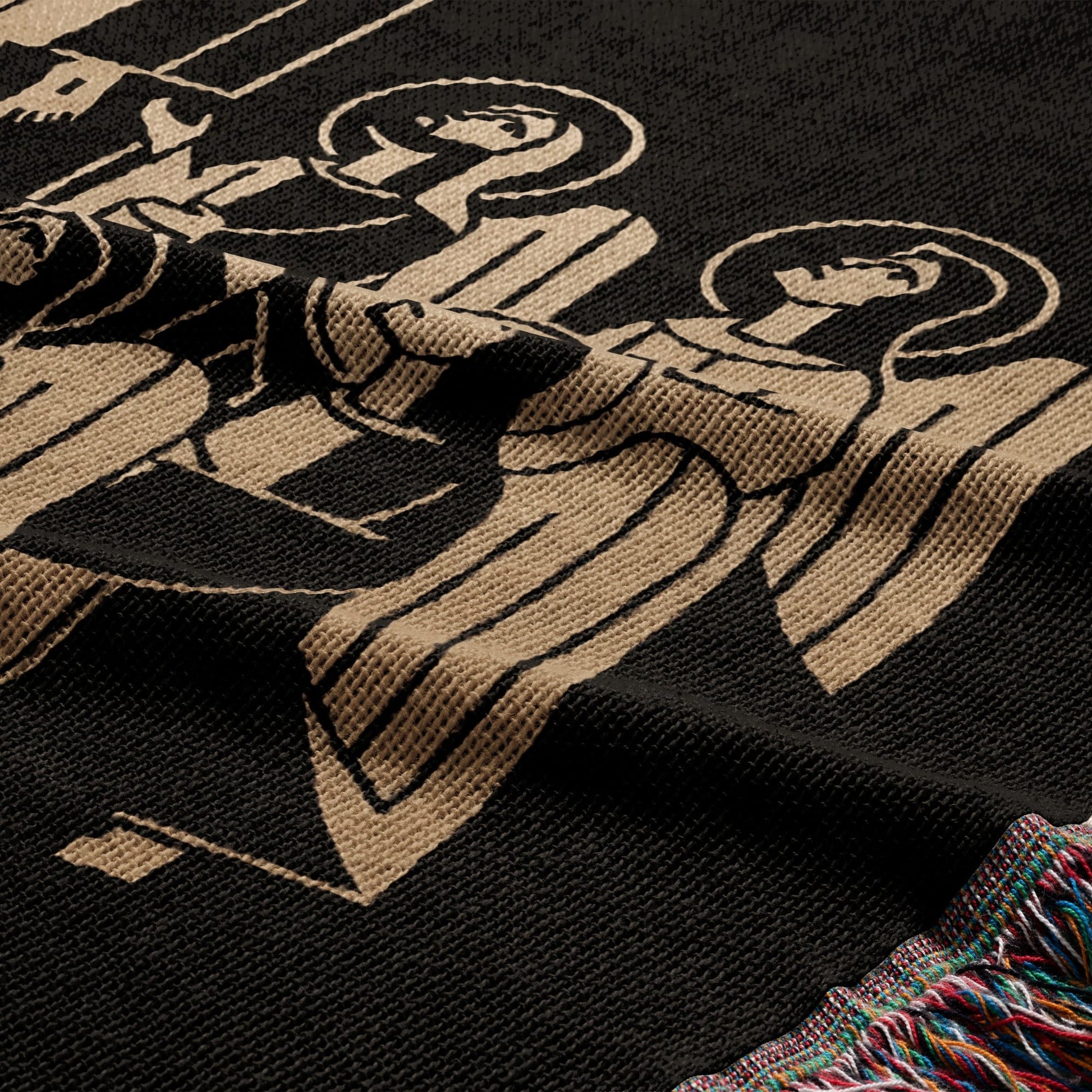 Black woven blanket with tan stylized angelic figures and fringed edge.