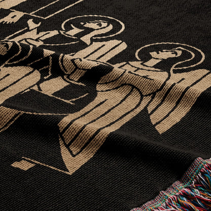 Black woven blanket with tan stylized angelic figures and fringed edge.