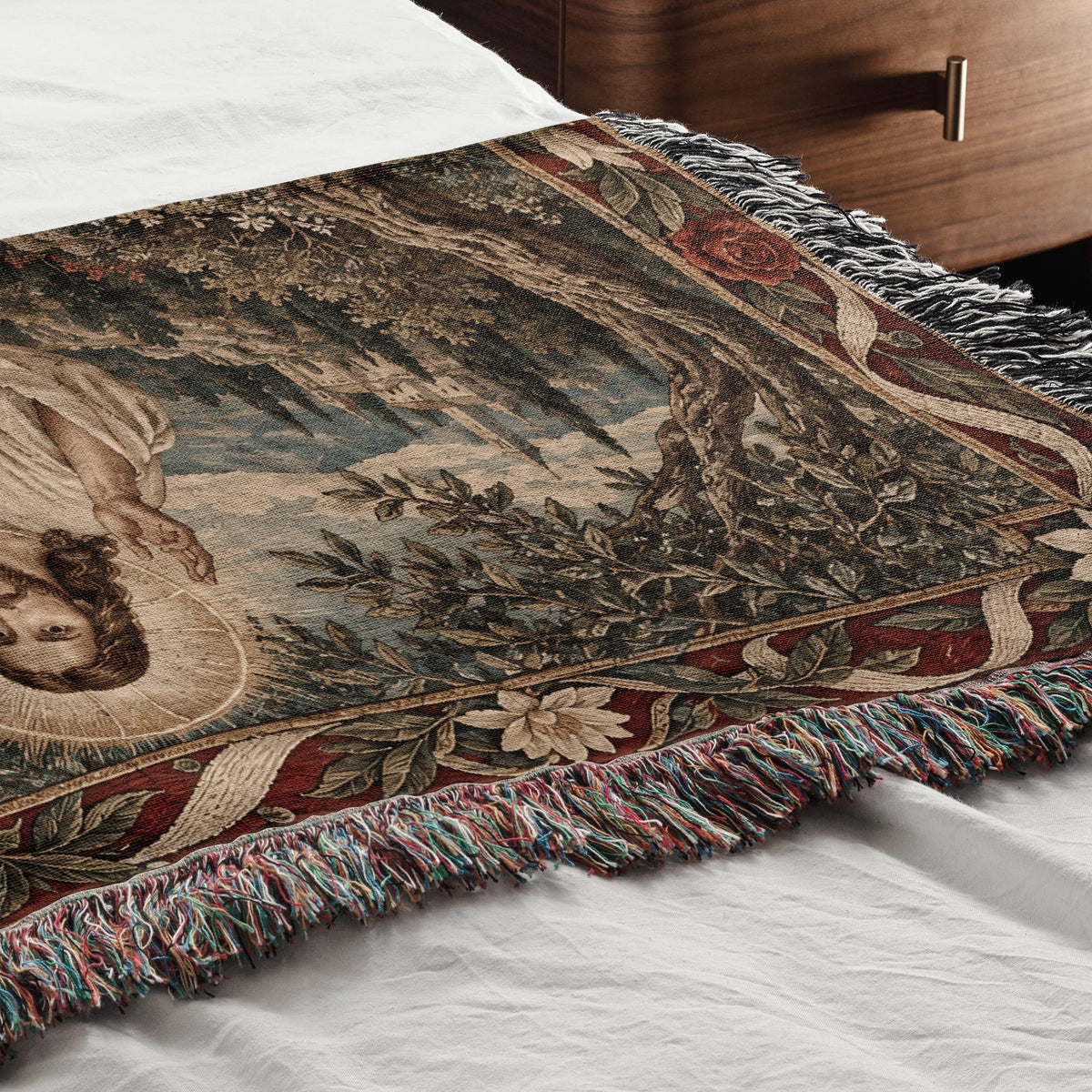 A woven blanket with a classical religious tapestry design rests on a white bedspread.