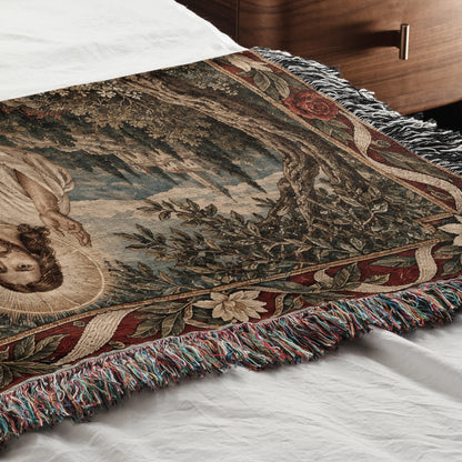 A woven blanket with a classical religious tapestry design rests on a white bedspread.