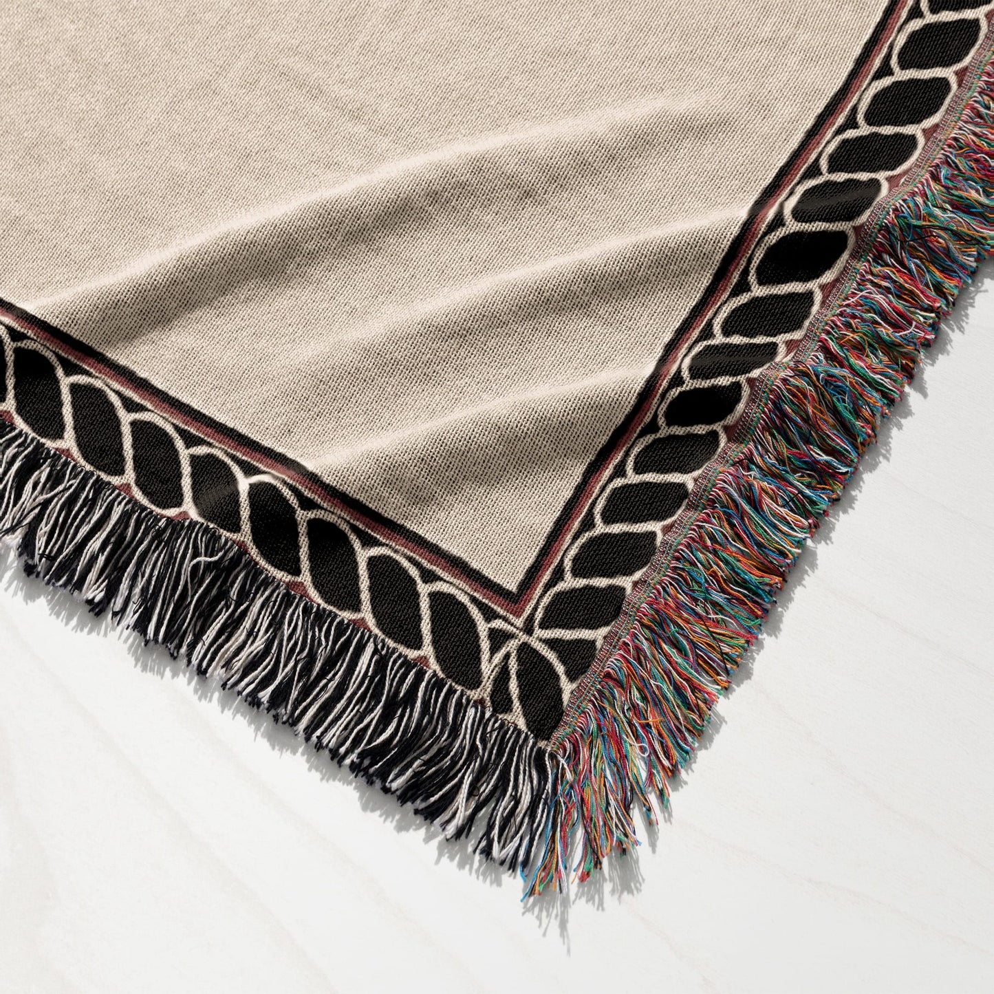 Beige throw blanket with black and red geometric border and colorful fringe.