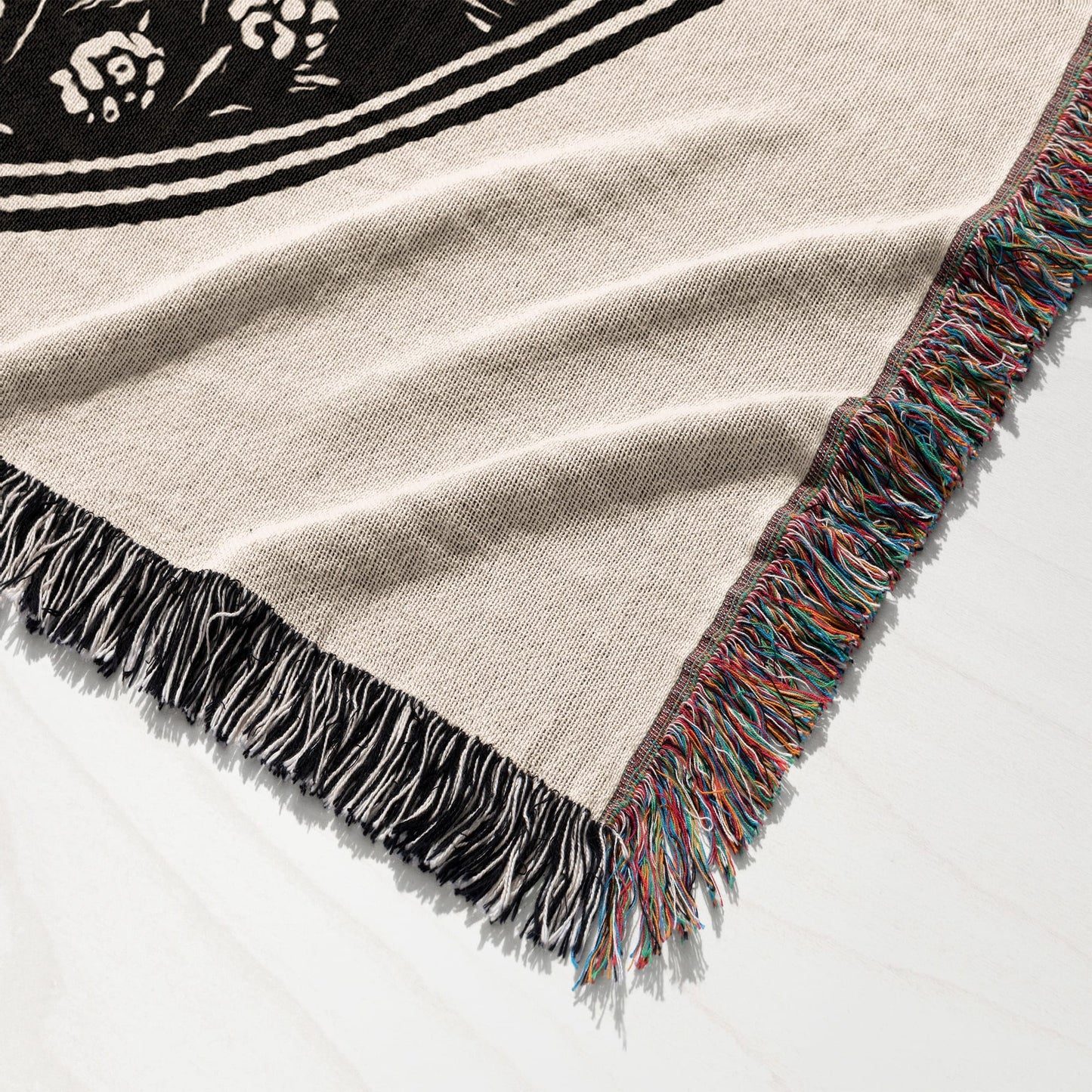 Woven blanket with fringe and a black floral design on a light background.