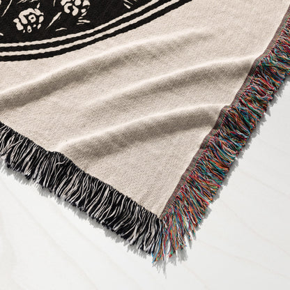 Woven blanket with fringe and a black floral design on a light background.