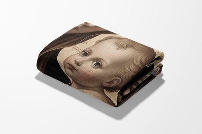 Tapestry depicting the Virgin Mary holding the infant Jesus, folded on a white surface.