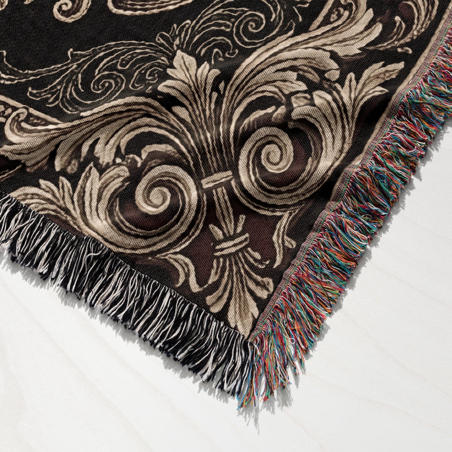 Black woven blanket with ornate gold and cream damask pattern and colorful fringe.