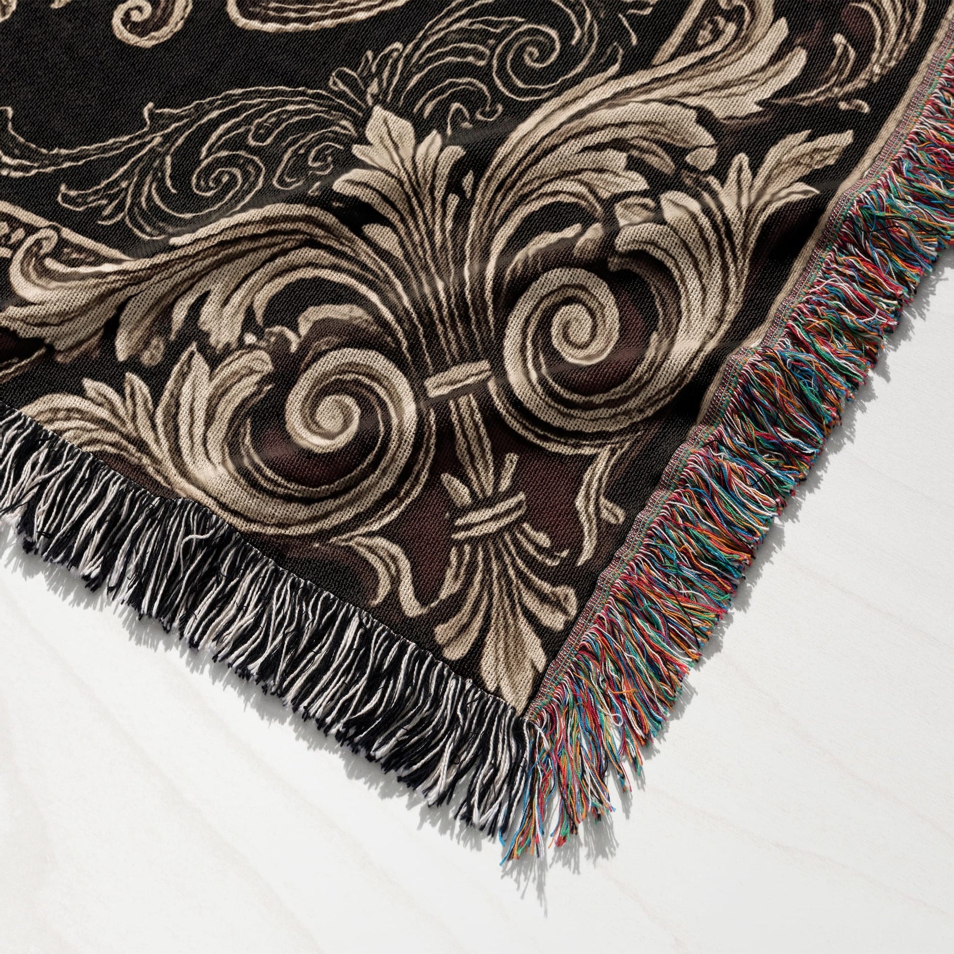 Black woven blanket with ornate gold and cream damask pattern and colorful fringe.
