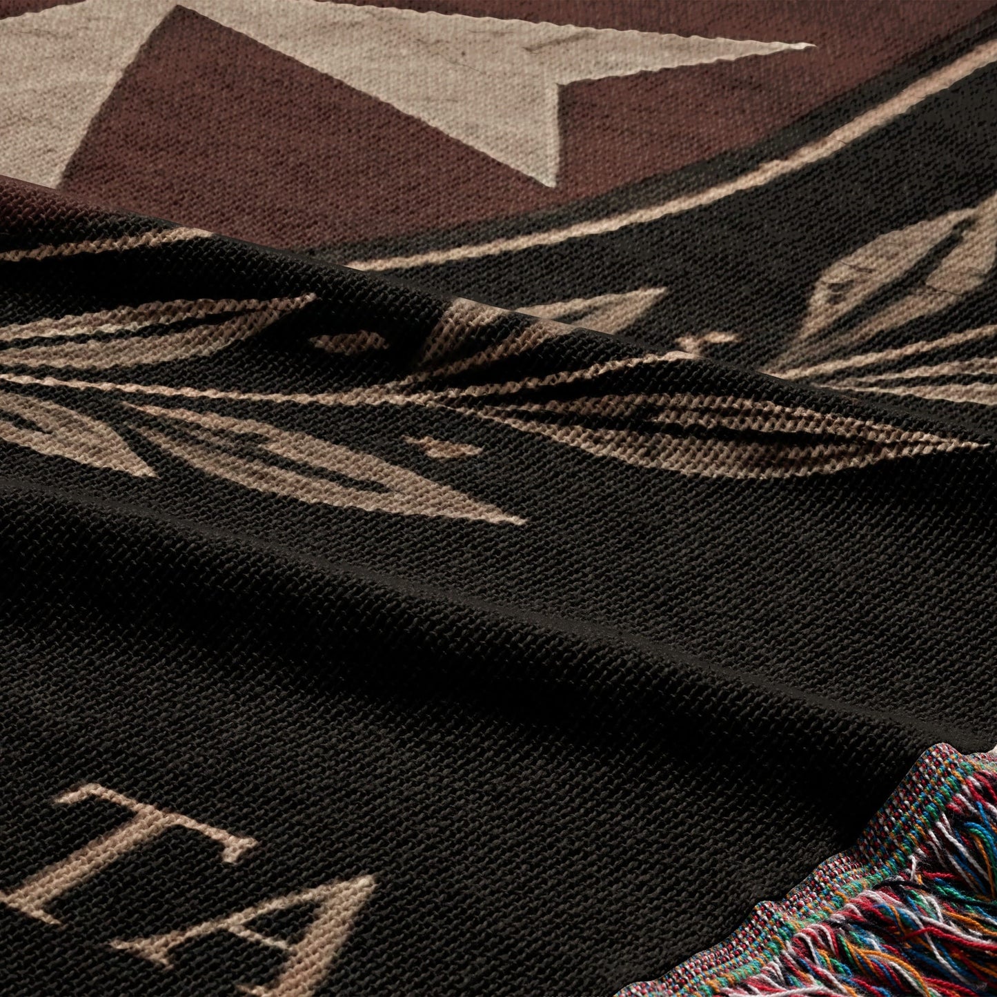 Black woven blanket with ornate border and the letter "T".