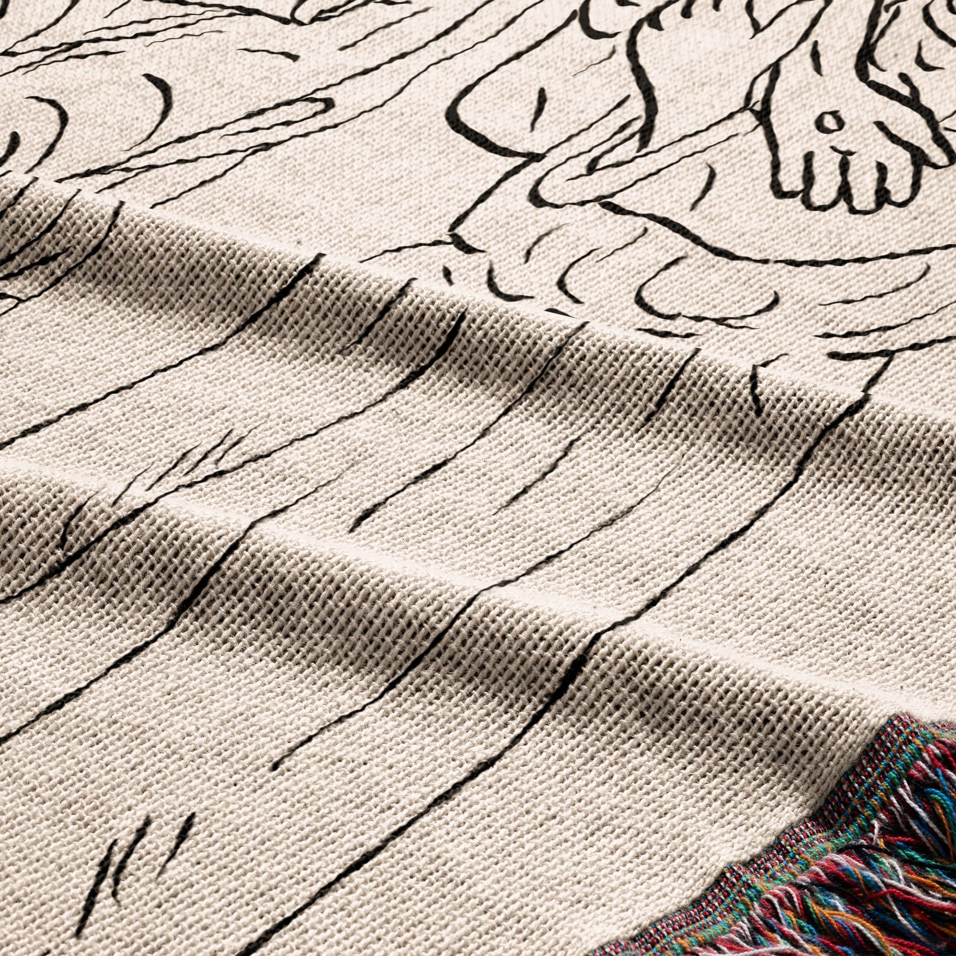 Close-up of a knitted throw blanket with a black line drawing design and a fringed edge.