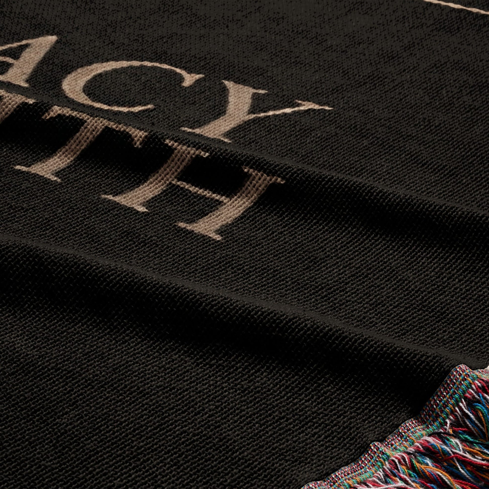 Black textile with "ACY" and "TH" in tan text and fringed multicolor edge.