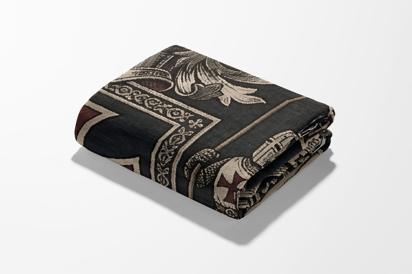 Folded blanket with dark tapestry pattern featuring cross emblems and ornate designs.