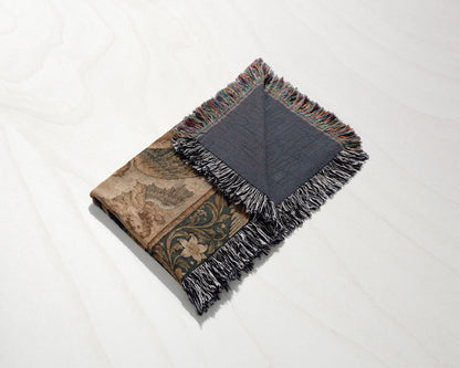 A folded woven throw blanket with a floral pattern and fringed edges on a light surface.