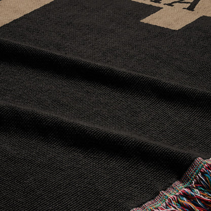 Black woven blanket with colorful fringe and partial letter text.