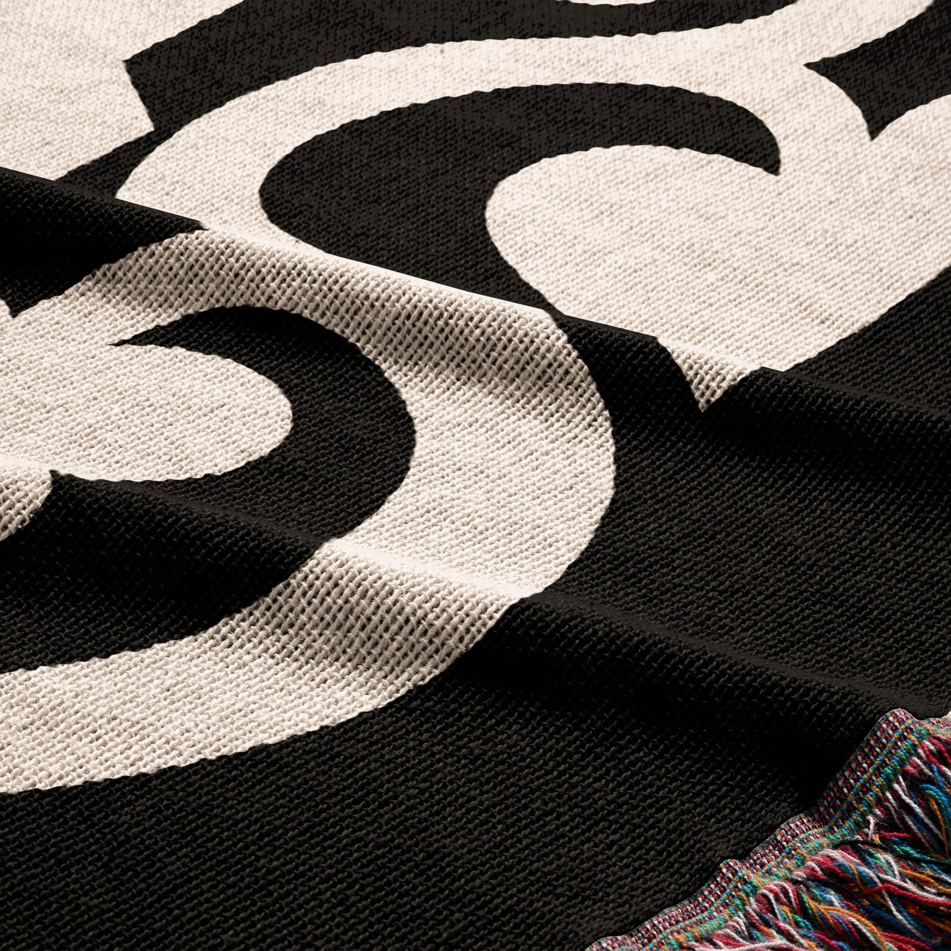 Black woven throw blanket with large white graphic pattern and tasseled edges.