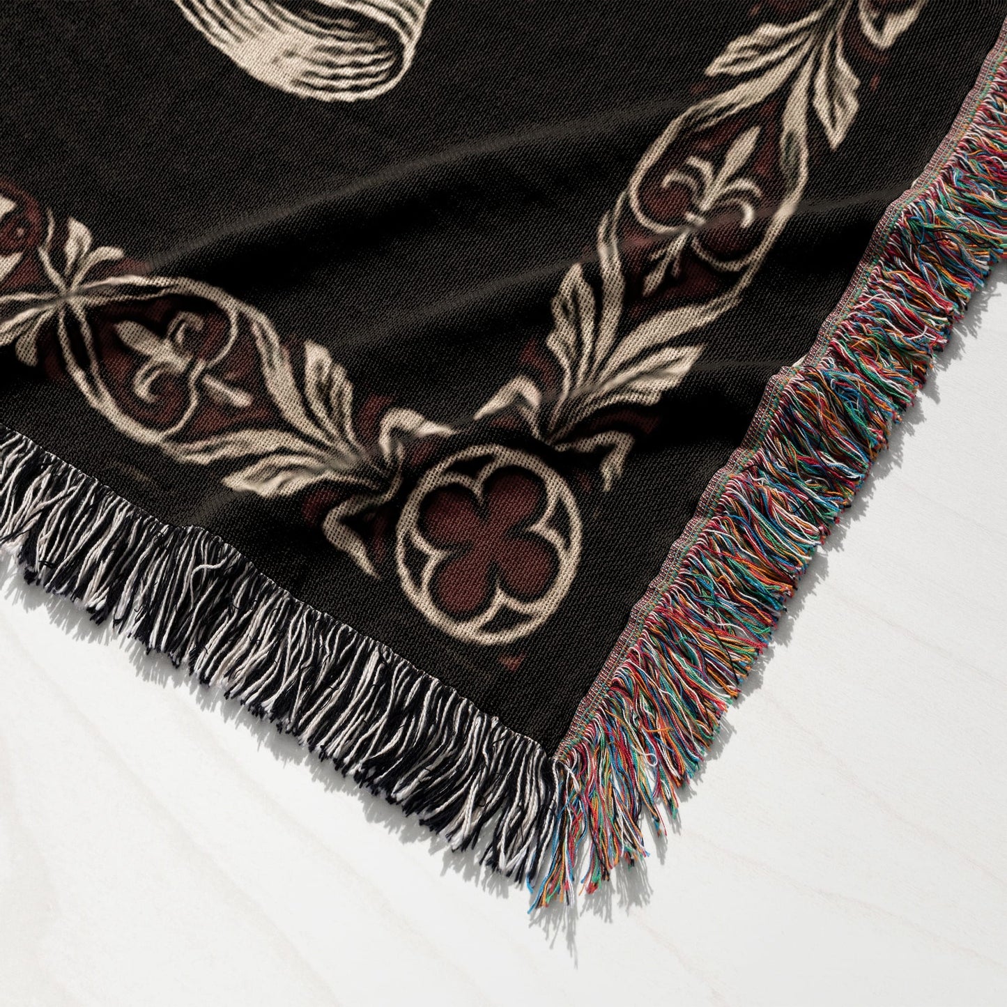 Black woven throw blanket with ornate filigree pattern and multi-colored fringe.