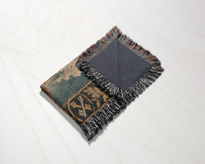 A folded woven tapestry throw blanket with a medieval design featuring crossed keys and fringe edges.