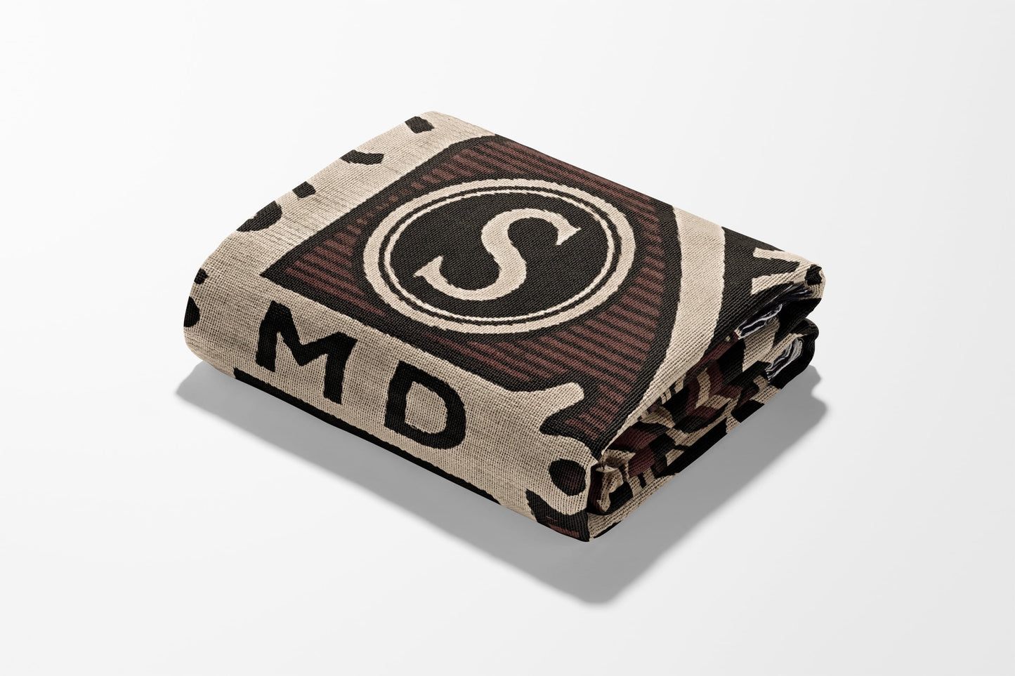 Folded blanket with beige, black, and brown geometric pattern featuring the letter S.