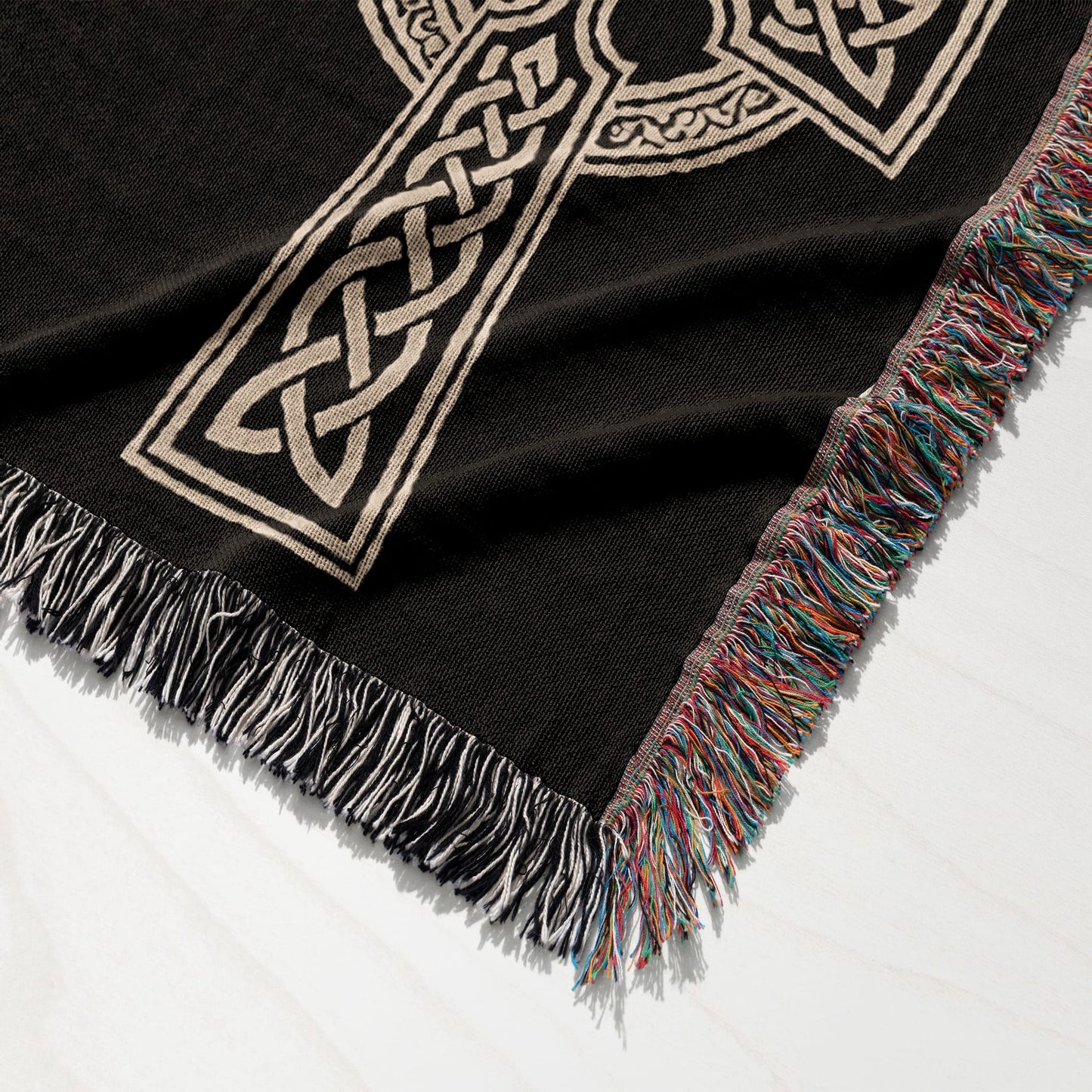 Black woven throw blanket with intricate beige Celtic knot design and fringed edge.