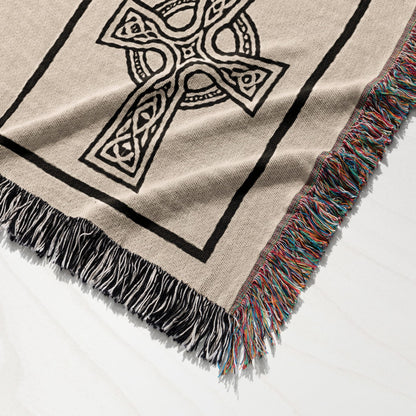 Beige woven throw blanket with a black Celtic knot cross design and colorful fringed edges.