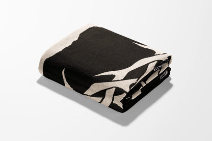 Folded black blanket with abstract cream pattern on white background.