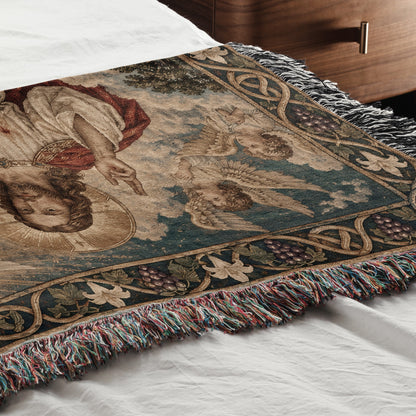 A woven throw blanket with a religious tapestry design featuring Jesus and angels lies on a bed.