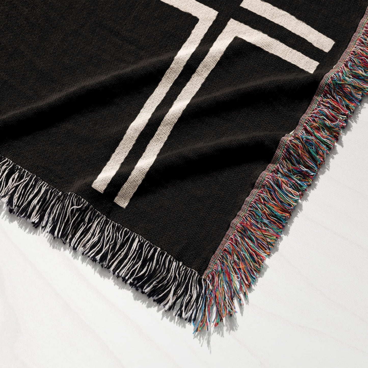 Black throw blanket with cream stripes and colorful fringe.