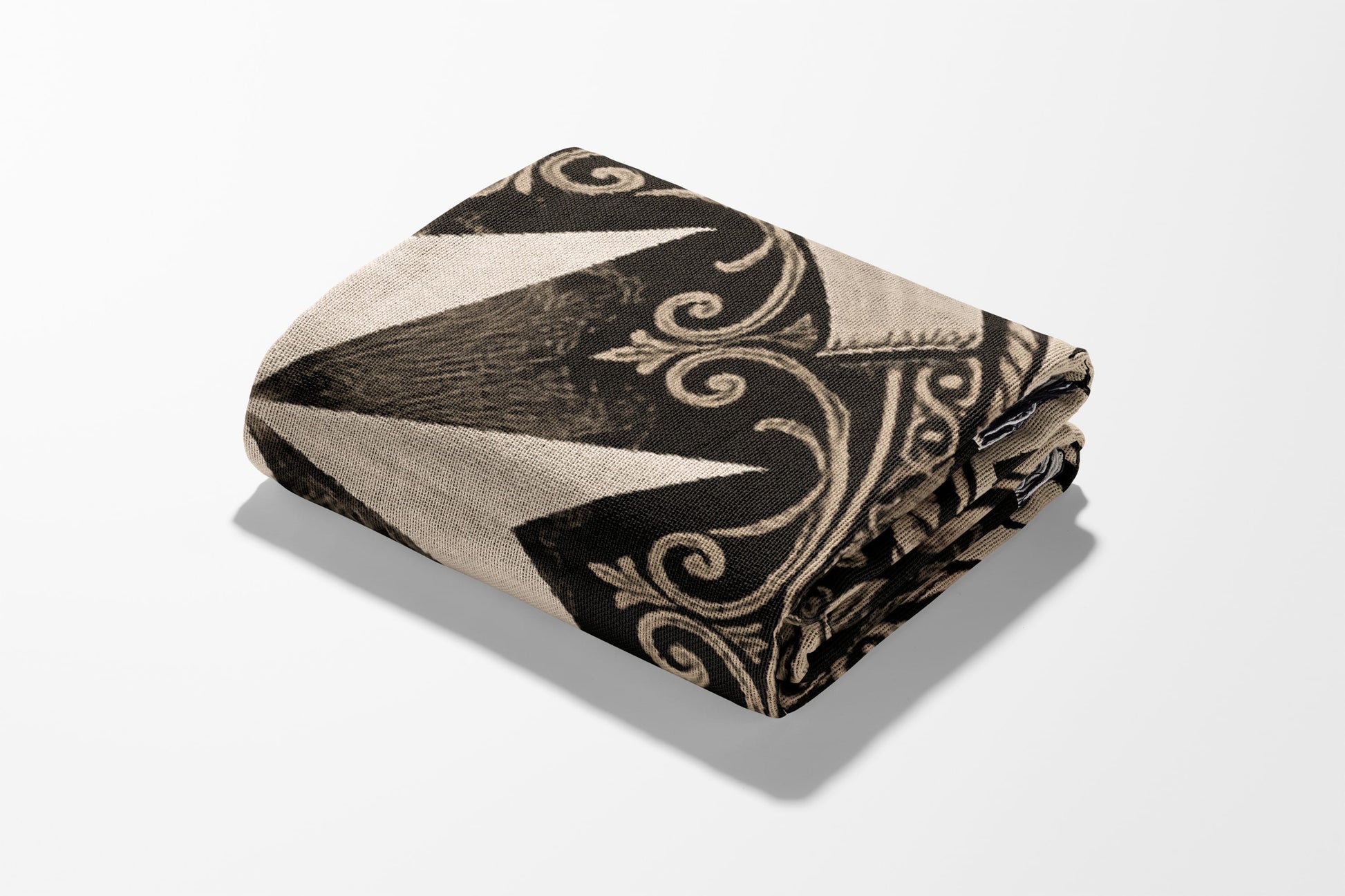 Folded blanket with black, beige geometric and scroll pattern on white background.