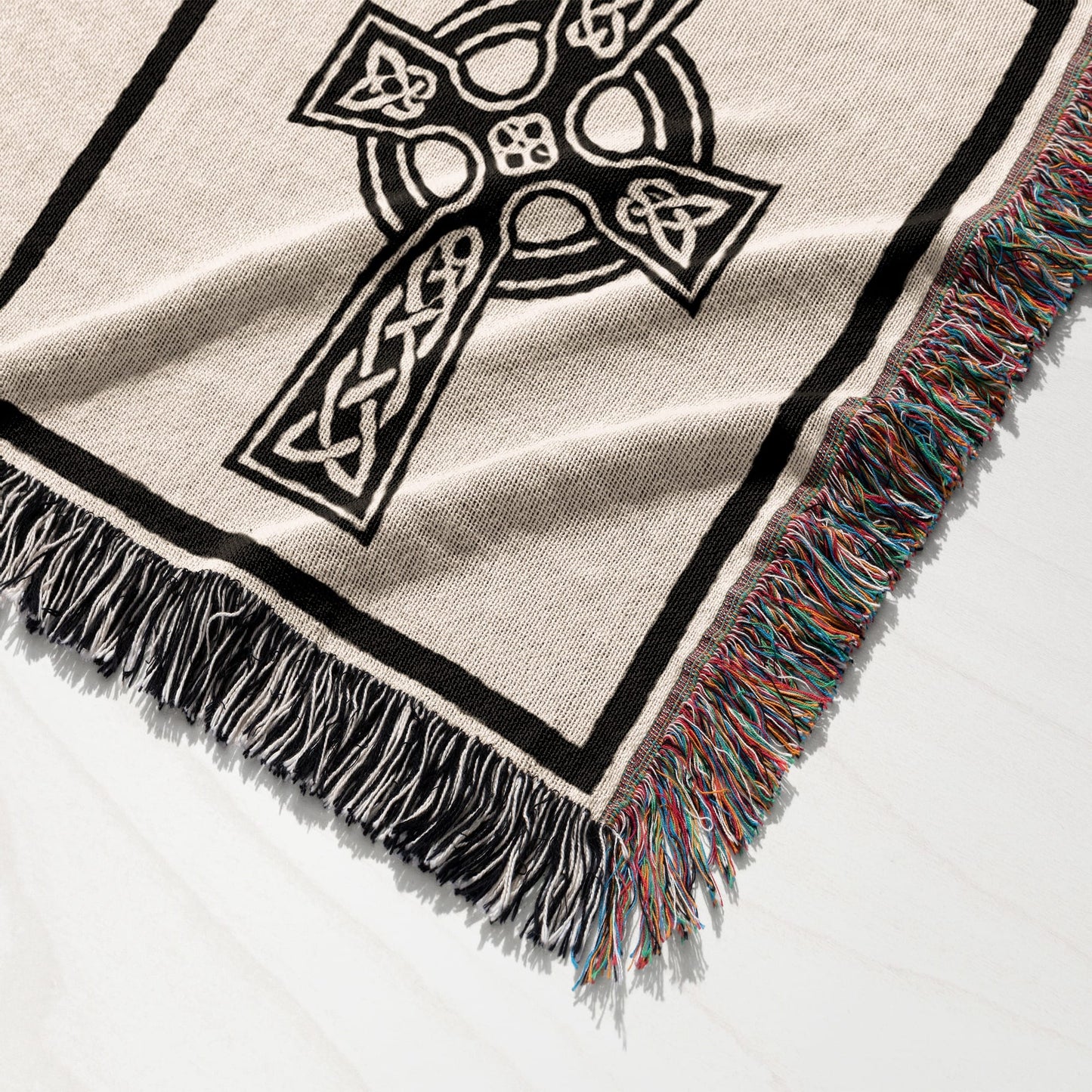 Woven throw blanket with a black Celtic cross design and multicolored fringed edges.